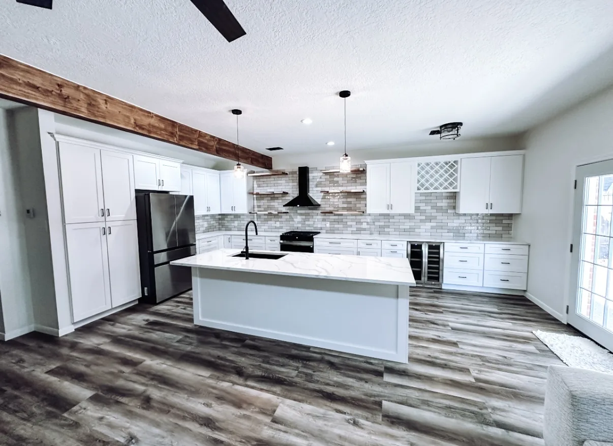 Remodeled custom kitchen by Texan Home Additions, Greater Houston, with white shaker cabinets, quartz waterfall island, rustic wood ceiling beam, and matte-black range hood