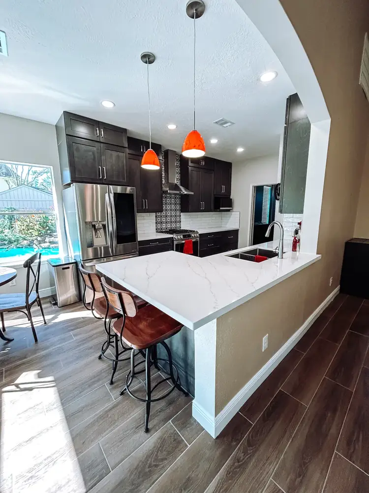Remodeled kitchen with espresso shaker cabinets, white quartz peninsula, orange glass pendants, and a backyard pool view