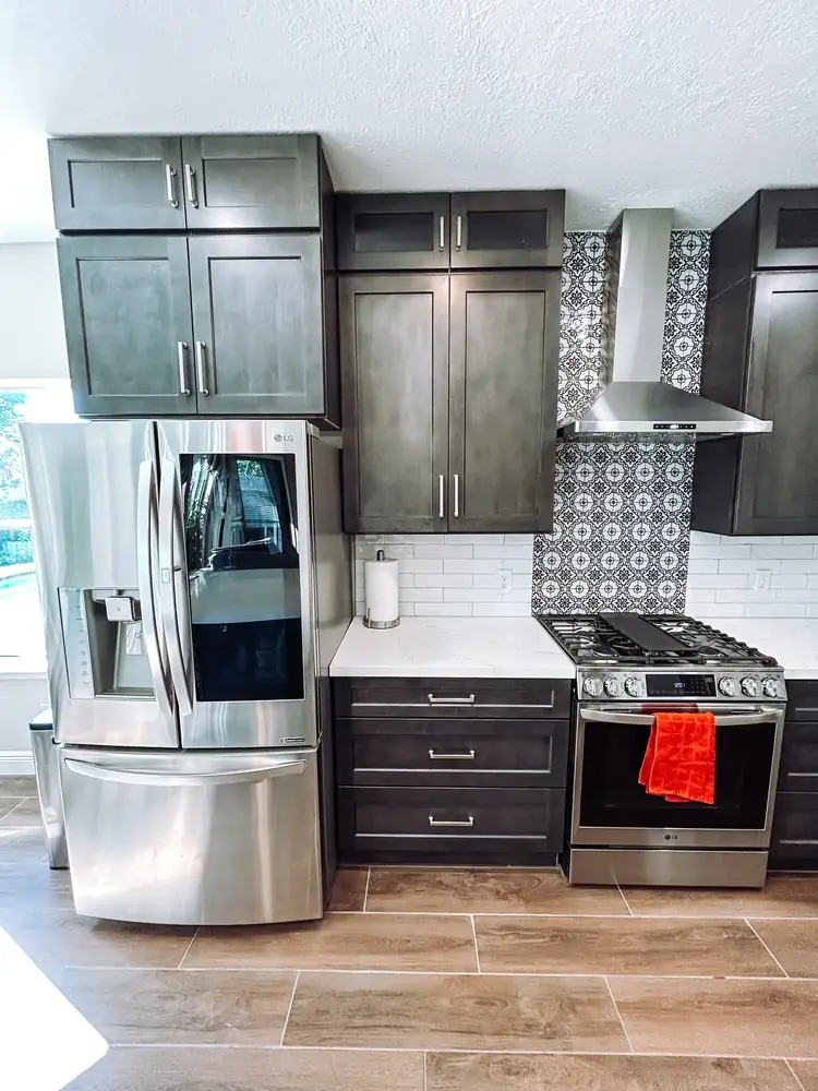 Dark gray kitchen cabinets with stainless appliances and black-and-white patterned accent tile behind the range hood