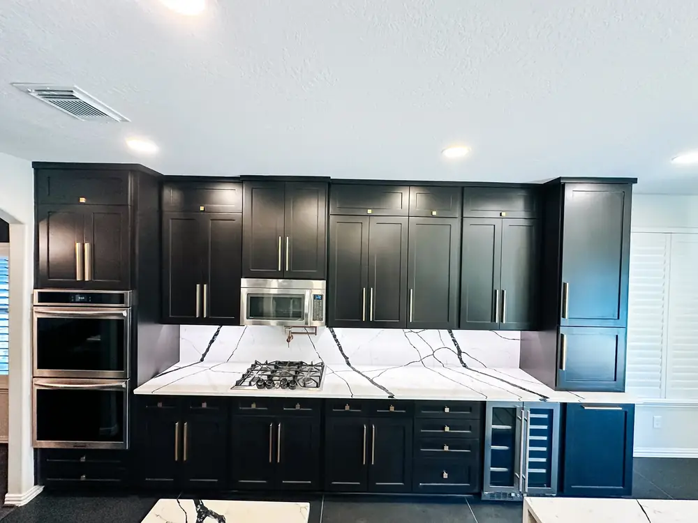Premier kitchen remodel with floor-to-ceiling black cabinetry, brass hardware, double wall ovens, and bold veined quartz backsplash