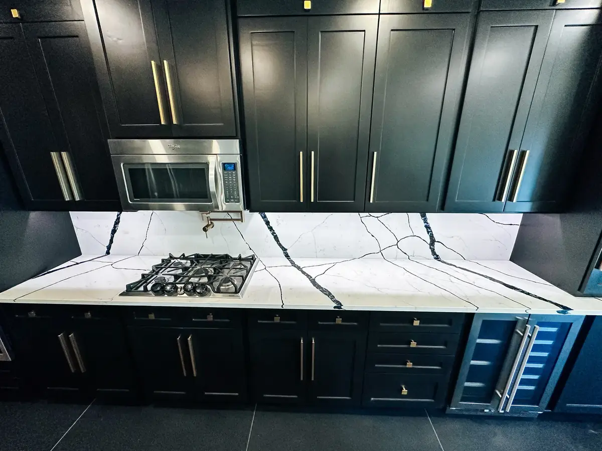 Black shaker cabinets with brass hardware, dramatic black-veined quartz countertop and full-height quartz backsplash in a high-end kitchen remodel by Texan Home Additions